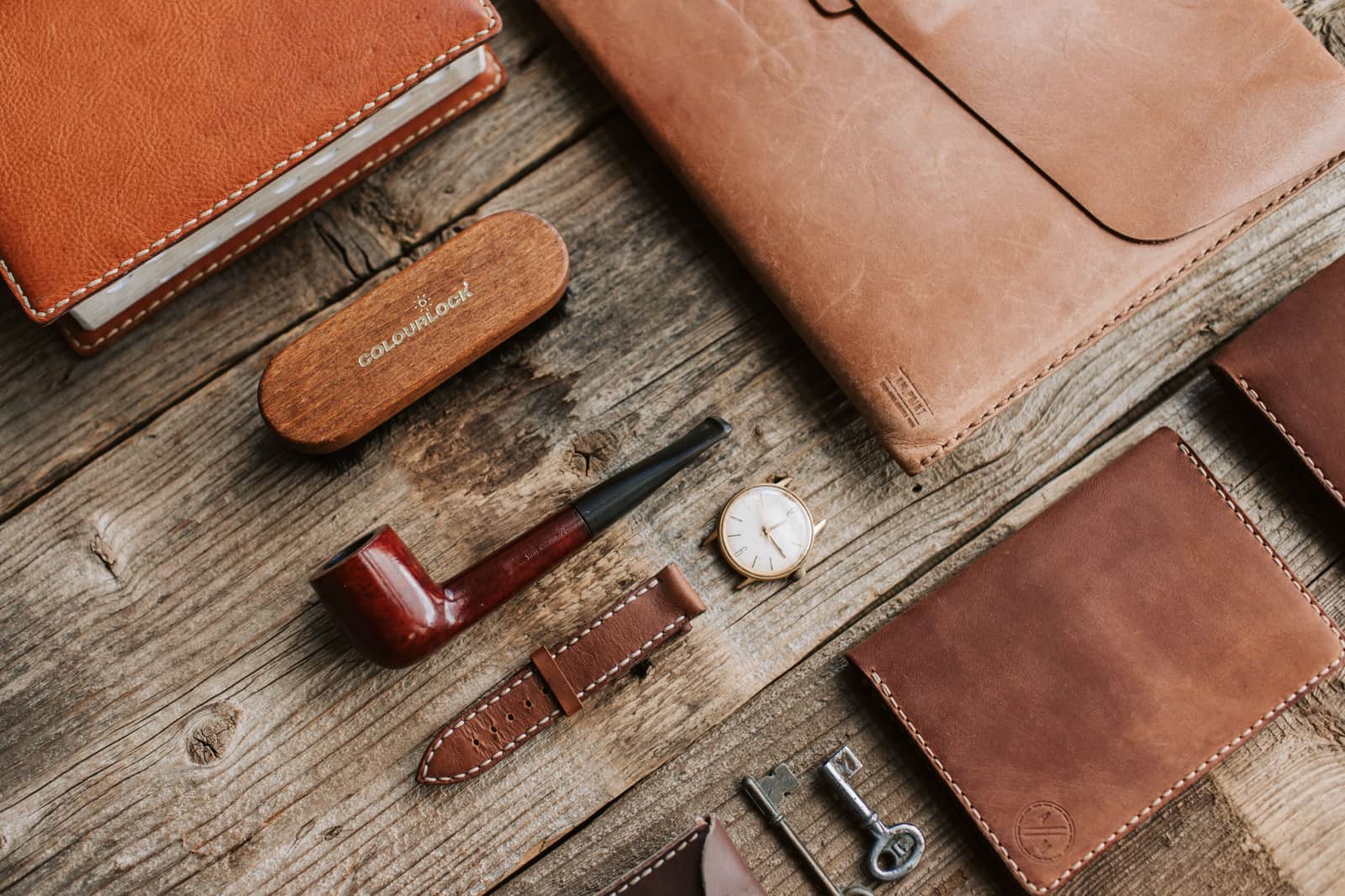 A close-up of brown leather goods and small accessories on a warm wooden surface